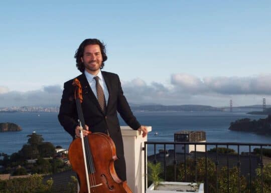 Músico con violonchelo en terraza con vista panorámica de San Francisco, ideal para eventos, conciertos al aire libre y festivales en vivo.