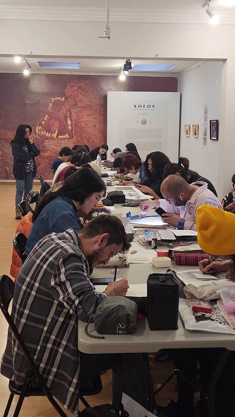 Personas participando en taller artístico en galería de arte, creando y aprendiendo técnicas de dibujo y pintura, promoviendo la educación artística en Colombia.