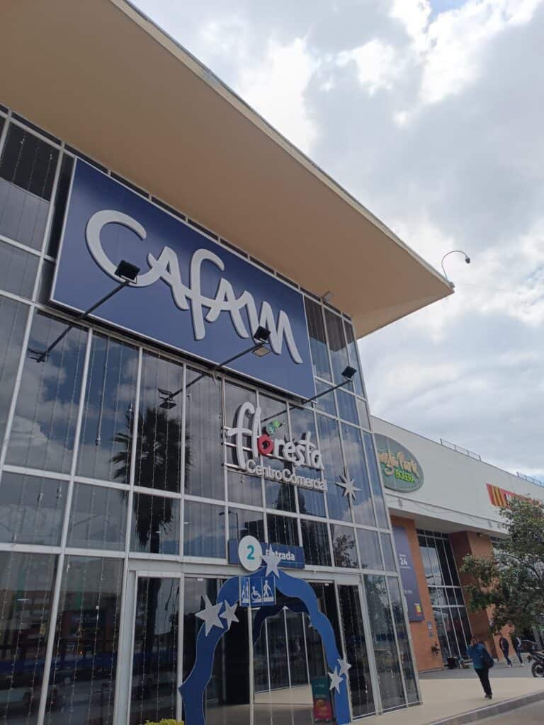 Contenedor de tiendas con señalización de entrada y decoraciones navideñas en un centro comercial moderno.