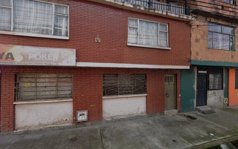 Edificio en zona urbana con ventanas seguras y fachada de ladrillo, puerta metálica y grafiti. Espacio residencial y comercial en ciudad colombiana, con infraestructura moderna y segura.
