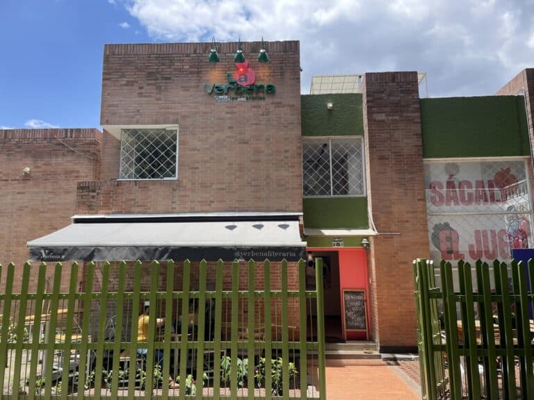 Alfombra verde, edificio de ladrillo con ventanas de reja, espacio restaurante abierto, ambiente colorido y acogedor en Medellín.