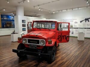 Vehículo clásico de color rojo en exhibición de museo en un espacio moderno con información y artefactos históricos sobre violencia y paramilitarismo en Colombia.