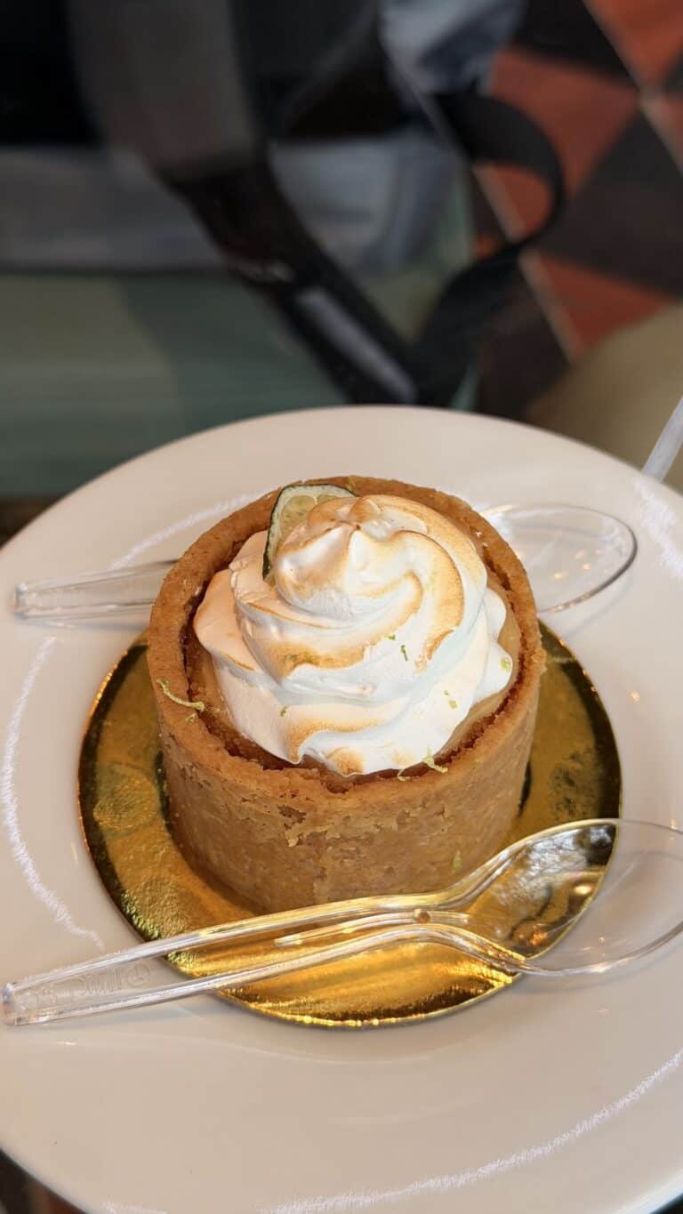 Tarta de arequipe con crema en un plato, decorada con una espiral de crema y acompañada de cucharas, en un ambiente de restaurante.