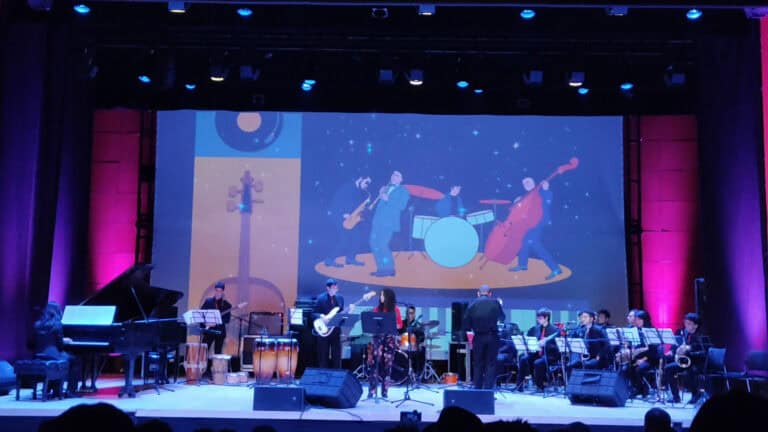 Imagen de un concierto en el Auditorio Mario Laserna, con una banda tocando en vivo en un escenario equipado con instrumentos y luces.