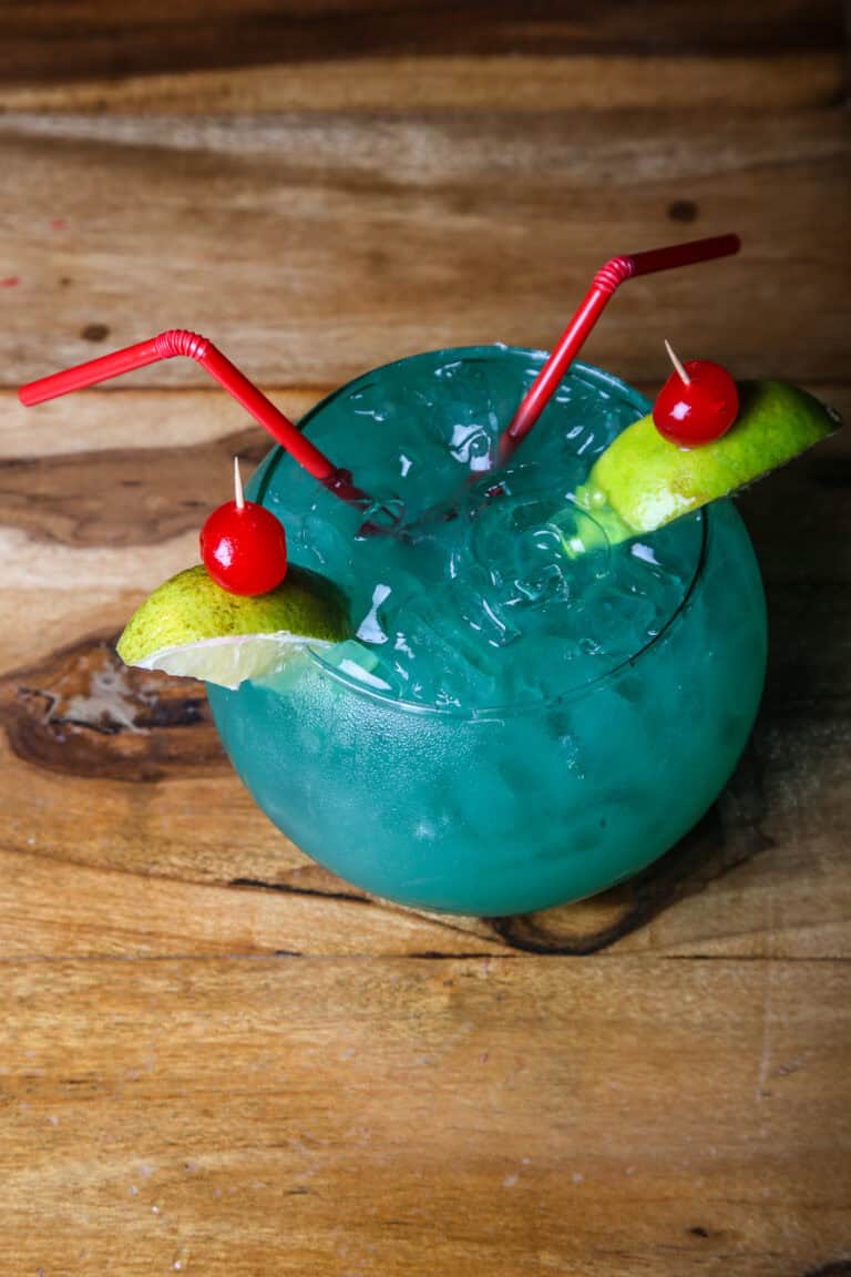Bebida refrescante de color azul en un vaso con hielo, decorada con cerezas y rodajas de limón, ideal para disfrutar en Crab's Bar.