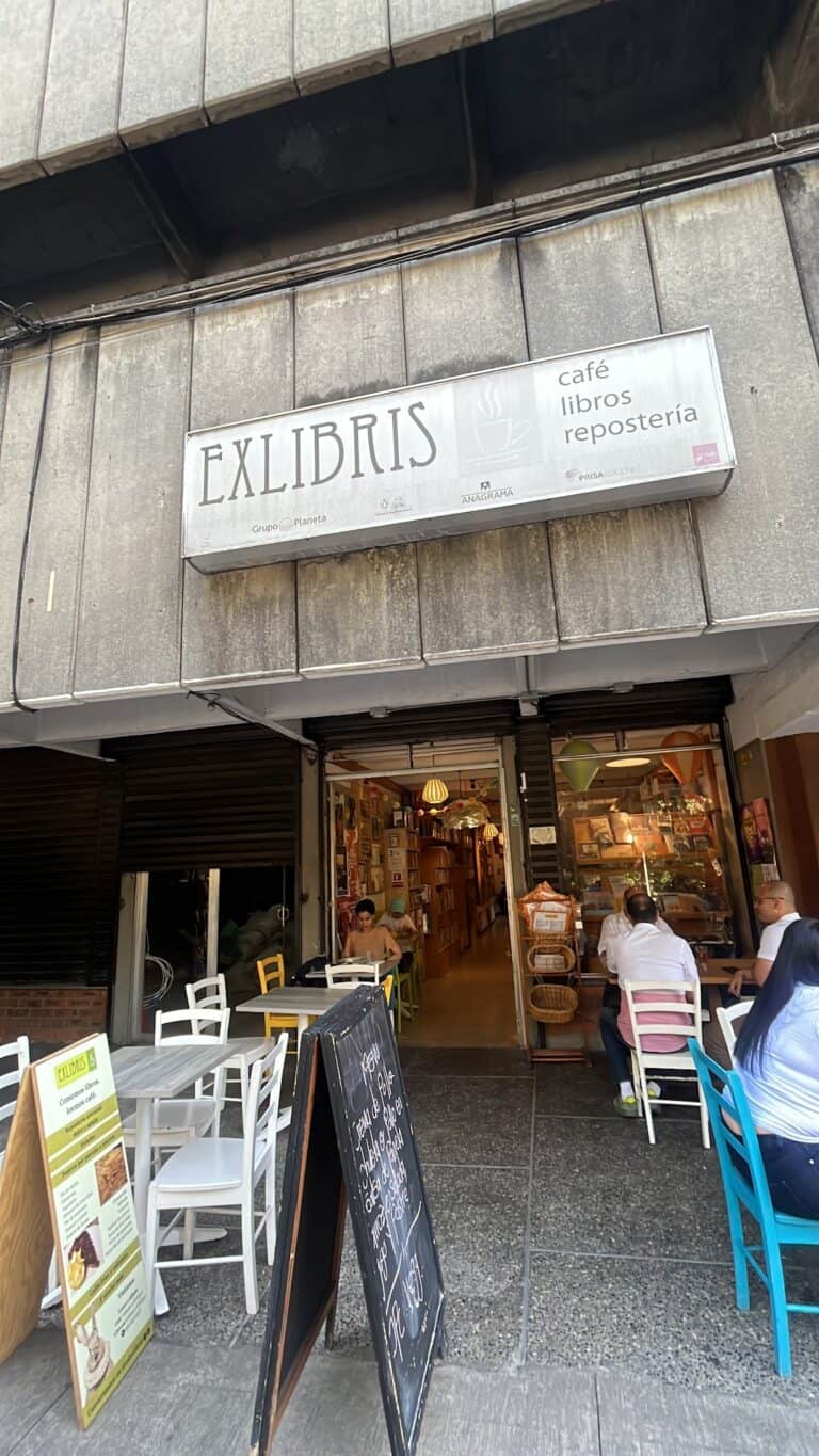 Fachada de Exlibris, cafetería con libros y repostería, en una calle urbana, con clientes disfrutando del ambiente acogedor y la oferta cultural y gastronómica.