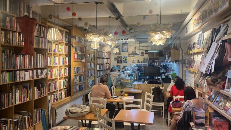 Personas disfrutando de café, libros y repostería en un acogedor espacio de librería y cafetería.