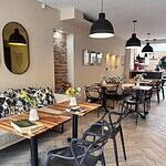 Ambiente de estar cómodo y elegante con mesas de madera, sillas negras y decoración moderna en un restaurante con iluminación cálida y detalles decorativos.