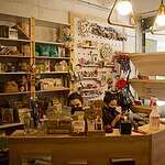 Amplia tienda con libros, productos de repostería y café, decorada con estanterías llenas de libros y artículos artesanales, creando un ambiente acogedor y cultural.