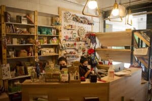 Amplia tienda con libros, productos de repostería y café, decorada con estanterías llenas de libros y artículos artesanales, creando un ambiente acogedor y cultural.