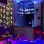 Bar con iluminación LED y estanterías con botellas de licor, ambiente moderno y colorido, ideal para eventos y reuniones sociales.