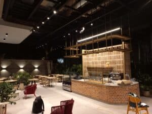 Amplia cafetería moderna en un evento campestre, con iluminación ambiental, mobiliario elegante y área de servicio con barra de ladrillo, ideal para eventos al aire libre y reuniones sociales.