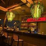 Interior de Listening Wine Bar con iluminación verde y estanterías llenas de vinos y vinilos, creando un ambiente acogedor para disfrutar de vinos y música en un espacio moderno.