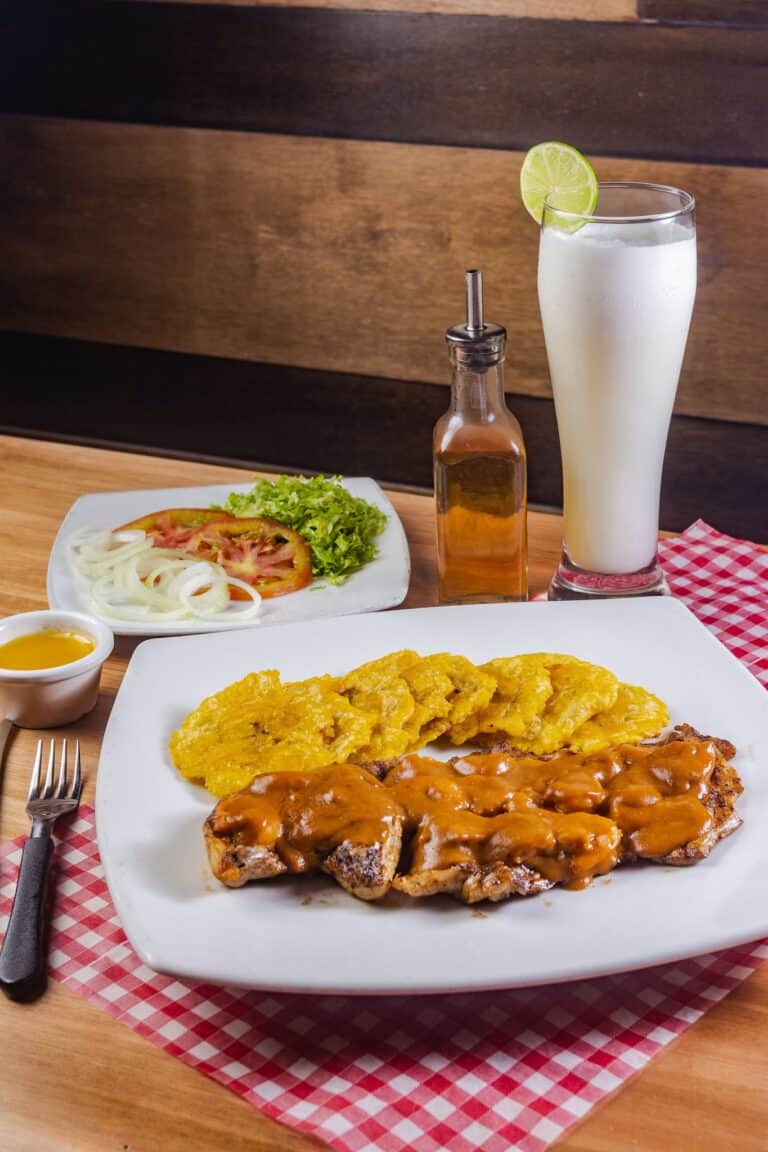 Filete de carne con salsa, papas fritas y ensalada fresca en restaurante El Santuario, acompañado de una bebida refrescante y una limonada, en un ambiente acogedor y tradicional.
