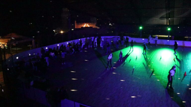 Patinaje en una pista de roller disco iluminada con luces verdes y azules, con varias personas disfrutando de la actividad en un ambiente vibrante y divertido durante la noche.