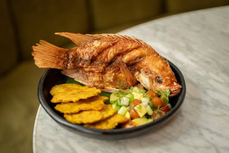 Pescado frito servido con ensalada fresca y patacones crujientes en Ana Restaurante Bar, un lugar ideal para disfrutar de comida deliciosa y ambiente acogedor en la ciudad.
