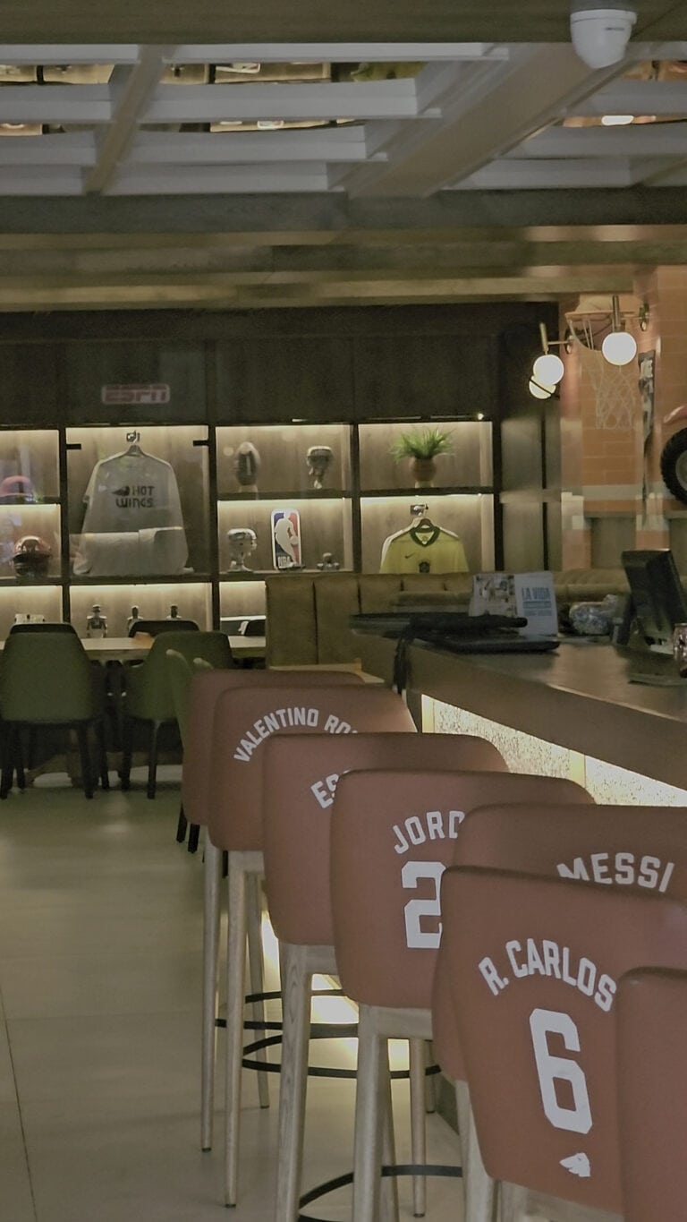 Interior de un restaurante con sillas con nombres de futbolistas, ambiente moderno y acogedor, ideal para disfrutar de comida y bebidas en un espacio cómodo.