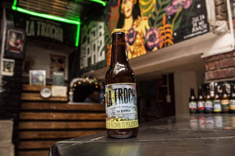 Botella de cerveza en un bar con decoración colorida y artística.