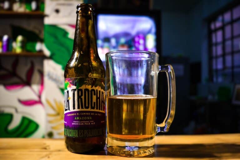 Cerveza artesanal La Trocha en botella y vaso, en un ambiente relajado y colorido, ideal para eventos y reuniones en La Casa de la Paz.