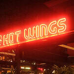 Cartel de neón con la frase "Hot Wings" iluminando un restaurante nocturno, ideal para amantes de las alitas picantes y la comida rápida en un ambiente vibrante y acogedor.
