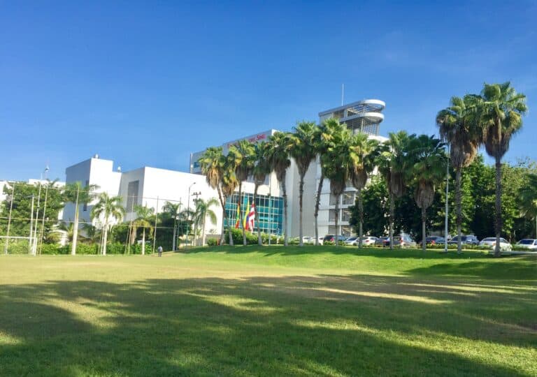 Vista exterior de la Universidad del Sinú en la sede Santillana, con áreas verdes y palmeras, en un día soleado.