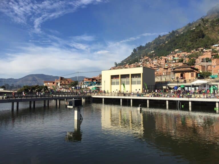 Vista del Lago de Guatapé con la estructura de la UVA de la Armonía y el paisaje montañoso de fondo, en un día soleado y despejado.