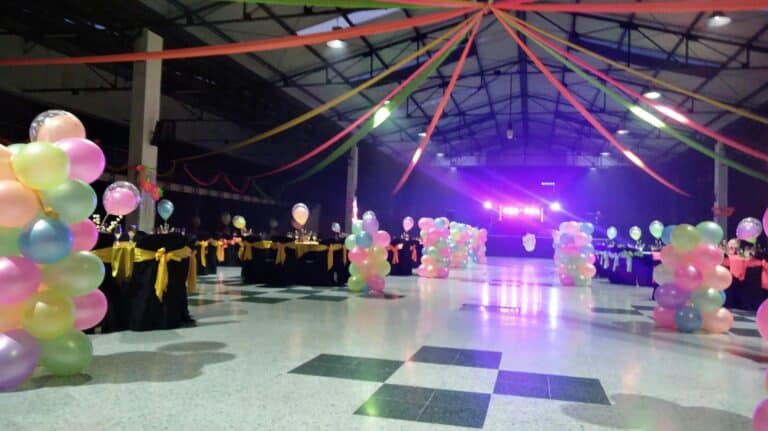 Espacio decorado en un centro de exposiciones con globos y cintas de colores para una celebración o evento especial.