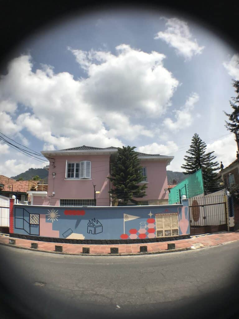Fachada de una casa en Colombia decorada con un mural colorido que incluye elementos abstractos y formas geométricas, en un día soleado con cielo parcialmente nublado.