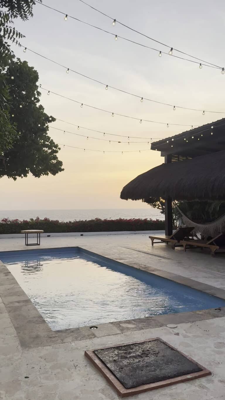 Imagen de una piscina en Casa Punta con vista al mar, rodeada de áreas de descanso y decorada con luces colgantes, ideal para eventos y relajación en un entorno natural.