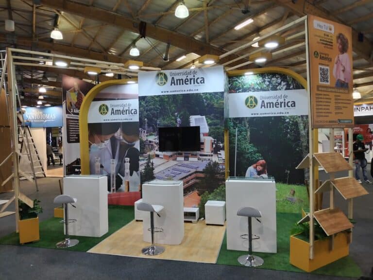 Espacio de exhibición de la Universidad de América en CORFERIAS Bogotá, con mobiliario moderno, pantallas y áreas de interacción para promover la educación superior.