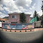 Fachada de una casa en Colombia con murales coloridos y un cielo nublado, en un entorno urbano con árboles y calles, reflejando arte y cultura local.