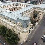 Vista aérea de la Facultad de Artes ASAB, un edificio histórico y emblemático en el centro de la ciudad, rodeado de árboles y calles concurridas, representando un importante centro cultural y educativ.