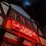 Neón rojo que muestra "La Roma Records" en la fachada de una tienda de discos en la noche, con cielo oscuro y luna visible, creando un ambiente vibrante y nostálgico.