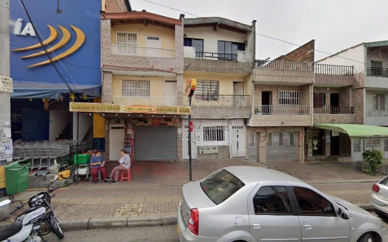 Fachada del sótano discoteca en Bogotá, con personas sentadas en la acera y vehículos estacionados en la calle, en un entorno urbano con edificios residenciales y comerciales.