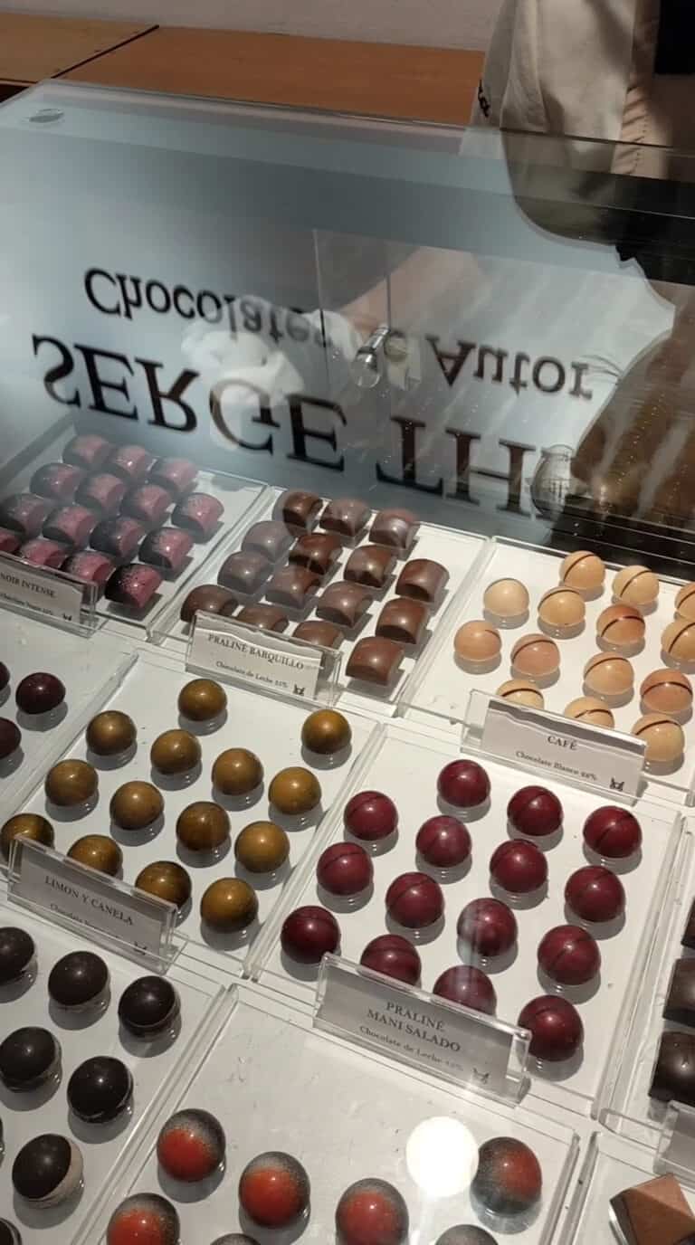 Selección de chocolates artesanales en diferentes sabores y colores en una vitrina, ideales para acompañar un café o como regalo en un ambiente de bar jazz y afines.