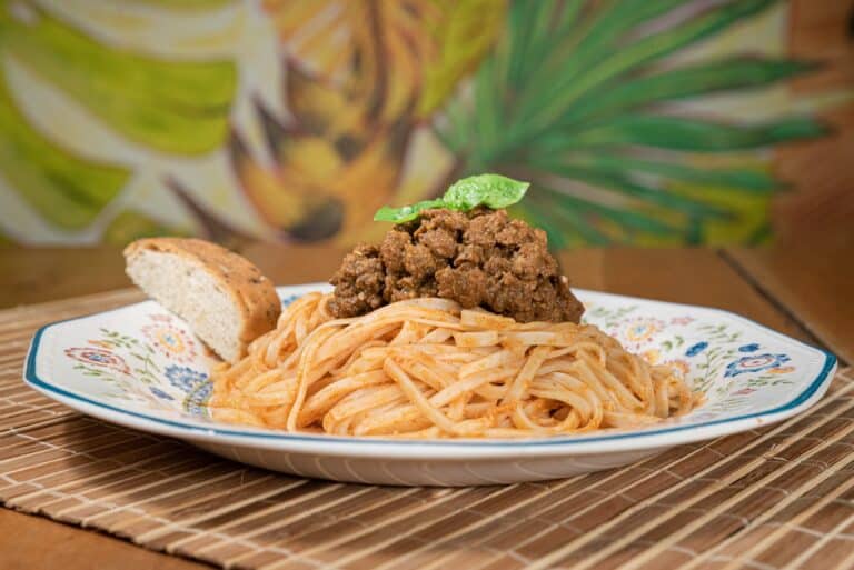 Plato de pasta con carne vegetal, acompañado de pan y decorado con hojas verdes, en un entorno de cocina vegetariana saludable y colorida.